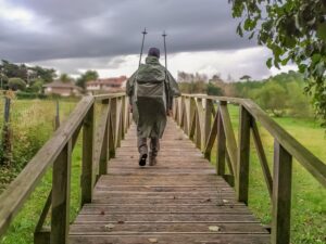 Mann wandert mit Stöcken in einem Regenponcho über eine Brücke